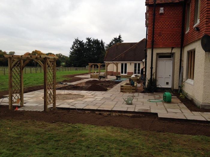 Most of the paving is now laid and reveals the large scale we are working to. The construction of the trellised arches gives this large space definition and shape. The garden also takes shape with the addition of the raised beds made from wooden sleepers – these are proving a popular trend. A circular area can be seen which will be infilled with a concrete base ready for a water feature to be installed at a later date and a large rectangular area of soil in the centre of the paving is made ready for turf to be laid.
