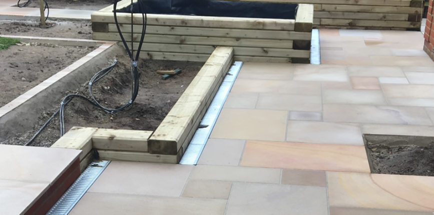 Showing the softwood sleepers with bevelled edges, complimenting the smart ACO drainage channels & subtles colours of the sawn Indian Sandstone paving.